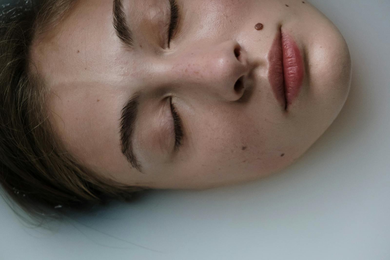 Close-up of a woman's face with closed eyes floating in water, showcasing tranquility.